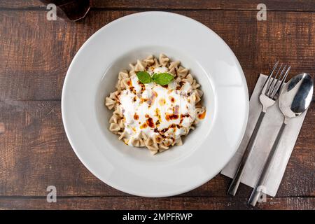 Kayseri ravioli oder Kayseri Mantisi auf einem weißen Teller auf einem Holztisch Stockfoto