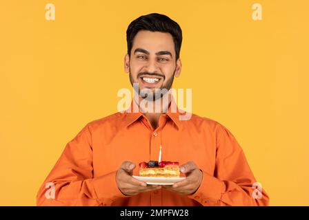 Porträt Von Happy Young Arab Man, Der Ein Stück Kuchen Mit Kerze Hält Stockfoto