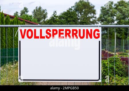 Eine rechteckige Tafel mit viel freiem Textplatz mit dem Wort VOLLSPERRUNG (Full Closure) auf einem Bauzaun. Stockfoto