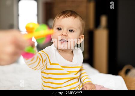 Mutter gibt ihrer kleinen Tochter Spielzeug, spielt mit einem kleinen Mädchen, mutter genießt Kinderbetreuung, sitzt im Bett Stockfoto