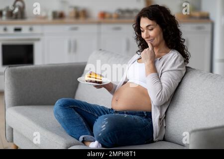 Schwangerschaftskrabbeln. Aufgeregte Schwangere Frau, Die Zu Hause Ein Stück Kuchen Hält Stockfoto