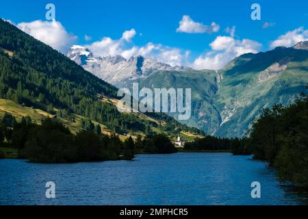 Blick über den Geschinersee bis zur Kirche Ulrichen, dem schneebedeckten Gipfel des Berges Galenstock in der Ferne. Stockfoto