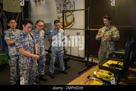 POLARIS POINT, Guam (18. Oktober 2022) – Navy Diver Seaman Jacob Swanson, dem U-Boot-Tender USS Emory S. Land zugeteilt (AS 39), Right, spricht mit Mitgliedern der Republic of Singapore Navy (RSN) in der Emergent Repair Facility während des RSN 4. und in den USA Navy Submarine Force Staff Talks, Oktober 18. Seit 2017 haben sich Leiter der US-amerikanischen U-Boot-Streitkräfte und der RSN-U-Boot-Streitkräfte zusammengeschlossen, um über eine verbesserte Interoperabilität und den Aufbau von Beziehungen zu diskutieren. Stockfoto