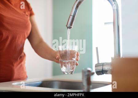 Unbekannte Frau, Die Glas Mit Wasser Aus Dem Wasserhahn In Der Küche Füllt Stockfoto