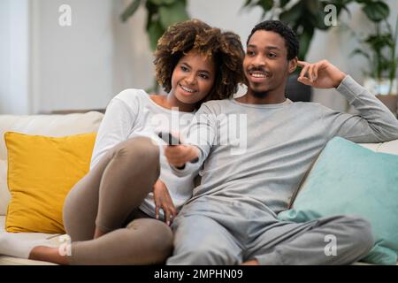 Glückliches afroamerikanisches liebevolles Paar, das zu Hause zusammen fernsieht Stockfoto