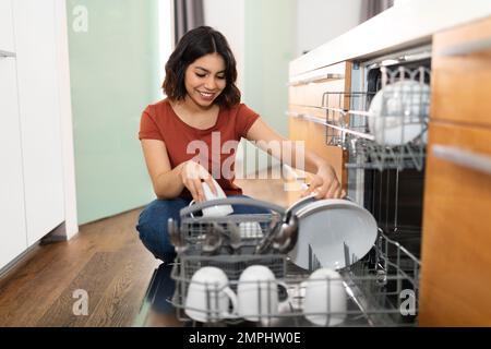 Porträt Einer Jungen, Glücklichen Frau Aus Dem Nahen Osten, Die Die Spülmaschine In Der Küche Entlädt Stockfoto