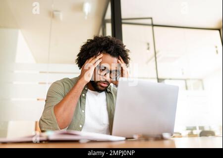 Konzentriert sich auf die Lösung von Aufgaben afroamerikanischer Freiberufler, der auf einen Laptop-Bildschirm im Büro starrt, ein nachdenklicher Geschäftsmann, der Märkte recherchiert, Aktien verkauft Stockfoto