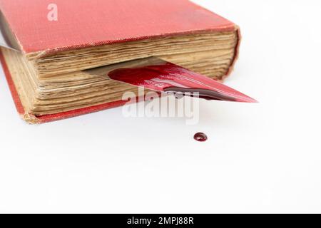 Blutiges Messer zwischen den Seiten eines alten Buches, mit tropfender roter Farbe, weicher Nahaufnahme Stockfoto