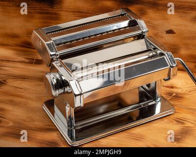 Handmaschine zum Rollen von Teig und Teigwaren. Nudelschneider. Verchromter Stahl. Eloxiertes Aluminium. Holzhintergrund. Stockfoto