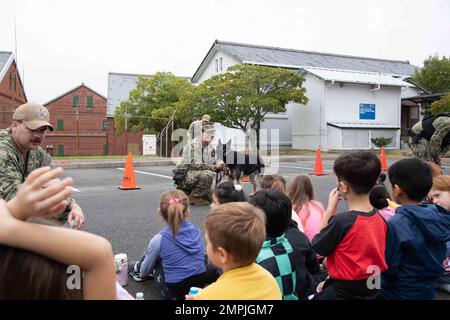 Master-at-Arms 1. Class Torye Cugal spricht mit Schülern der Sasebo Elementary School über militärische Arbeitshunde bei Commander, Fleet Activities Sasebo (CFAS) am 27. Oktober 2022. Die Studenten besuchten CFAS, um mehr über Techniken zu erfahren, die von der Sicherheitsabteilung verwendet werden, um die Community sicher und einsatzbereit zu halten. Stockfoto