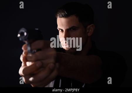 Professioneller Killer mit Waffe auf schwarzem Hintergrund Stockfoto