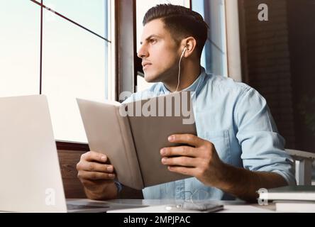 Ein Mann, der am Tisch im Café Hörbücher hört Stockfoto