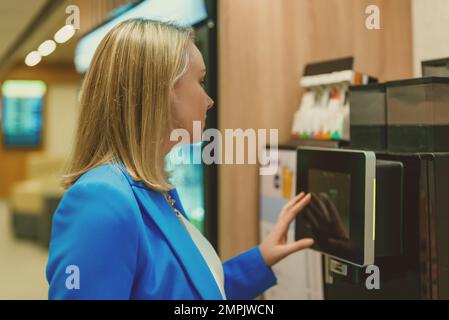 Frau im Business-Anzug, die Kaffee aus der Kaffeemaschine macht. Stockfoto