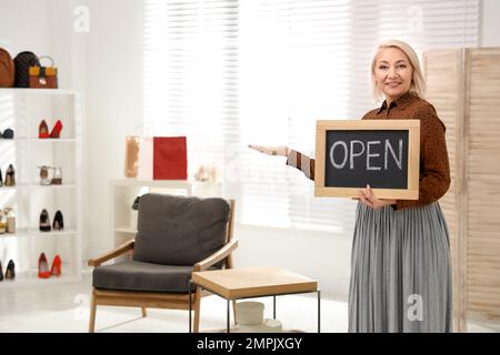 Weibliche Geschäftsinhaberin mit OFFENEM Schild in einer Boutique. Platz für Text Stockfoto
