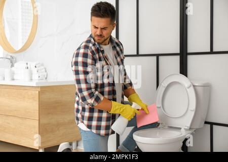 Junger Mann fühlt sich angewidert, als er die Toilettenschüssel im Bad reinigte Stockfoto