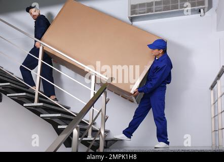 Professionelle Arbeiter, die Kühlschränke auf Treppen in Gebäuden tragen Stockfoto
