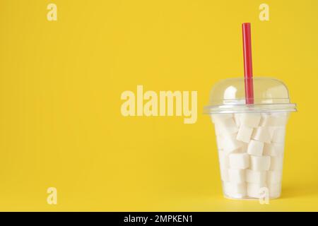 Raffinierte Zuckerwürfel im Kunststoffbecher mit Stroh auf gelbem Hintergrund. Platz für Text Stockfoto