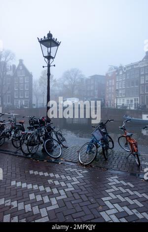 Blick über den Prinsengracht-Kanal, Amsterdam, Nordholland an einem nebligen Wintermorgen mit Fahrrädern, die auf der Straßenseite geparkt sind Stockfoto