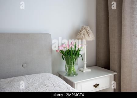 Wunderschöne rosa Tulpen Blumen in Vase neben Tischlampe auf Nachttisch im Schlafzimmer Stockfoto