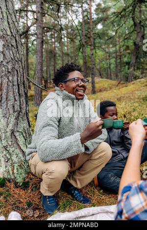 Glücklicher Vater, der Becher hielt, während er sich mit der Familie im Wald duckte Stockfoto