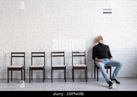 Ein erwachsener Mann, der auf einem Stuhl schläft, während er auf einen Stuhl neben der weißen Wand wartet Stockfoto