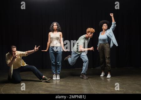 Die gesamte Länge junger multiethnischer Schauspieler, die in verschiedenen Posen auf der Bühne Proben Stockfoto