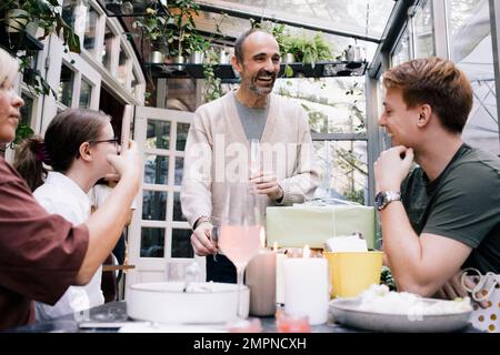 Glücklicher Mann, der eine Rede hielt, während er mit der Familie im Restaurant einen Drink hielt Stockfoto