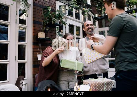 Seitenansicht des Mannes, der seiner Schwester ein Geschenk überreicht, während er im Restaurant steht Stockfoto