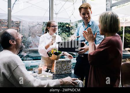 Lächelnder Mann öffnet Schuhkarton, während er mit Eltern im Restaurant spricht Stockfoto