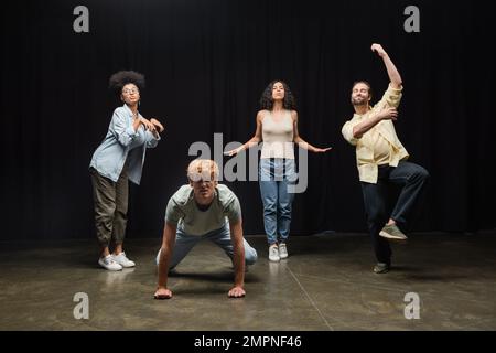 Die ganze Länge multiethnischer Schauspieler, die in verschiedenen Posen auf der Bühne im Theater Proben Stockfoto