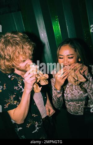 Junge Freunde essen Sandwiches, während sie im Nachtclub sind Stockfoto