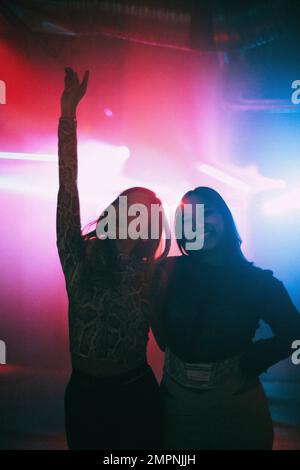 Porträt von glücklichen jungen Freundinnen, die mit Armen im Nachtclub stehen Stockfoto
