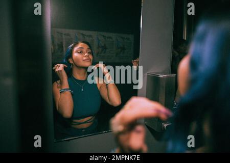 Reflexion einer jungen Frau, die Spiegelreflexion im Bad eines Nachtclubs betrachtet Stockfoto