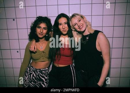 Porträt von jungen, multirassischen, weiblichen Freunden, die mit Armen gegen die weiße Wand im Nachtclub stehen Stockfoto