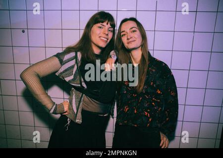 Porträt einer lächelnden Transgender-Frau mit einer Freundin, die im Nachtclub an der weißen Wand steht Stockfoto