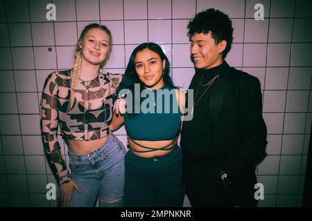 Porträt einer glücklichen jungen Frau, die mit Armen um einen nicht binären Freund an der weißen Wand steht Stockfoto