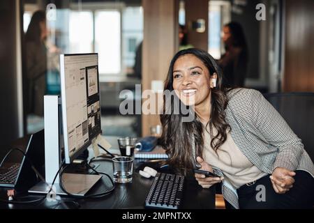 Glückliche Geschäftsfrau mit kabellosen InEar-Kopfhörern, die im Büro sitzt Stockfoto