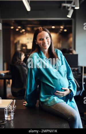 Porträt einer schwangeren Geschäftsfrau, die im Büro am Schreibtisch sitzt Stockfoto