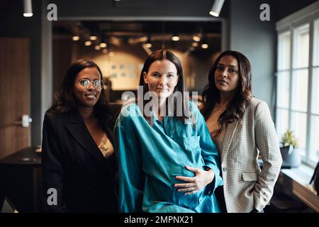 Selbstbewusste Geschäftsfrauen mit schwangeren Kollegen im Büro Stockfoto