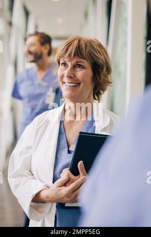Glückliche Ärztin blickt weg, während sie im Krankenhaus steht Stockfoto