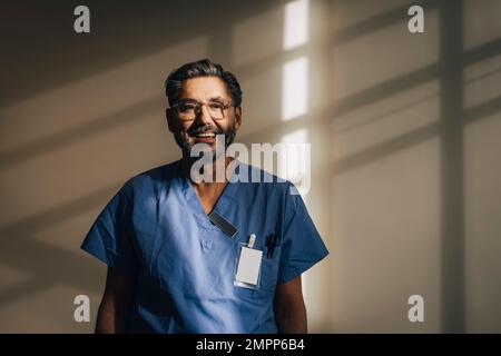 Porträt eines glücklichen männlichen Arztes, der im Krankenhaus an der Wand steht Stockfoto