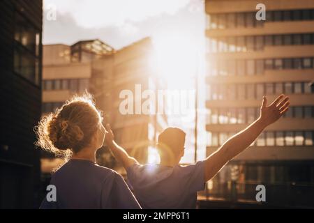 Rückansicht eines Arztes, der am sonnigen Tag mit ausgestreckten Armen eines Kollegen steht Stockfoto