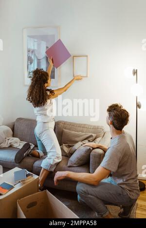 Seitenansicht eines Mannes, der seine Freundin mit einem Bilderrahmen an der Wand sieht Stockfoto