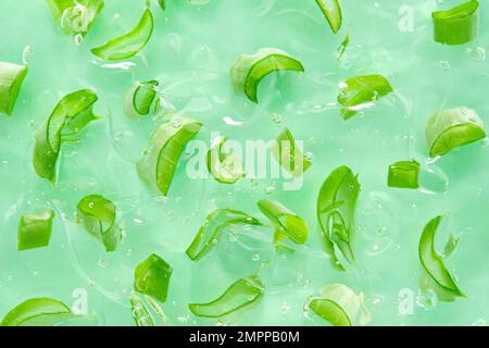 Aloe-Gel-Hintergrund mit Aloe-Scheiben. Schneiden Sie Scheiben von Aloe in transparentes kosmetisches Aloe-Gel. Flach verlegt. Draufsicht. Stockfoto