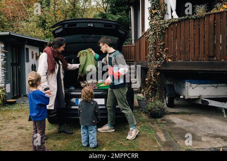 Die Familie bereitet sich auf das Picknick vor, während sie Sachen in den Kofferraum eines Elektroautos lädt Stockfoto