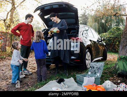 Lächelnde Mutter schenkt ihren Töchtern Getränke ein, während sie Freizeit beim Picknick verbringen Stockfoto