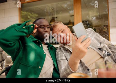 Multirassische männliche Freunde machen Selfie über Smartphone im Straßencafé Stockfoto