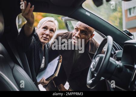 Verkäuferin mit Dokumenten, die männlichen Kunden Fahrzeugmerkmale erklären Stockfoto