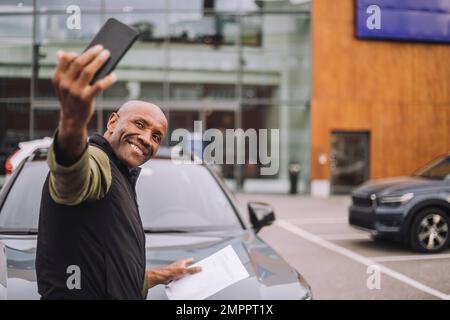 Glücklicher Mann, der nach dem Kauf eines neuen Autos Selfie über das Smartphone macht Stockfoto