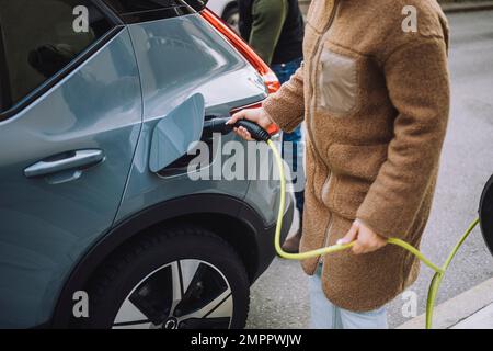 Mittelteil einer Frau, die ein Elektroauto an der Station auflädt Stockfoto